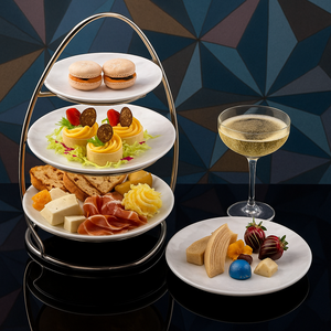 Uma bandeja de três andares e uma travessa separada com petiscos, pães doces e duas taças de espumante